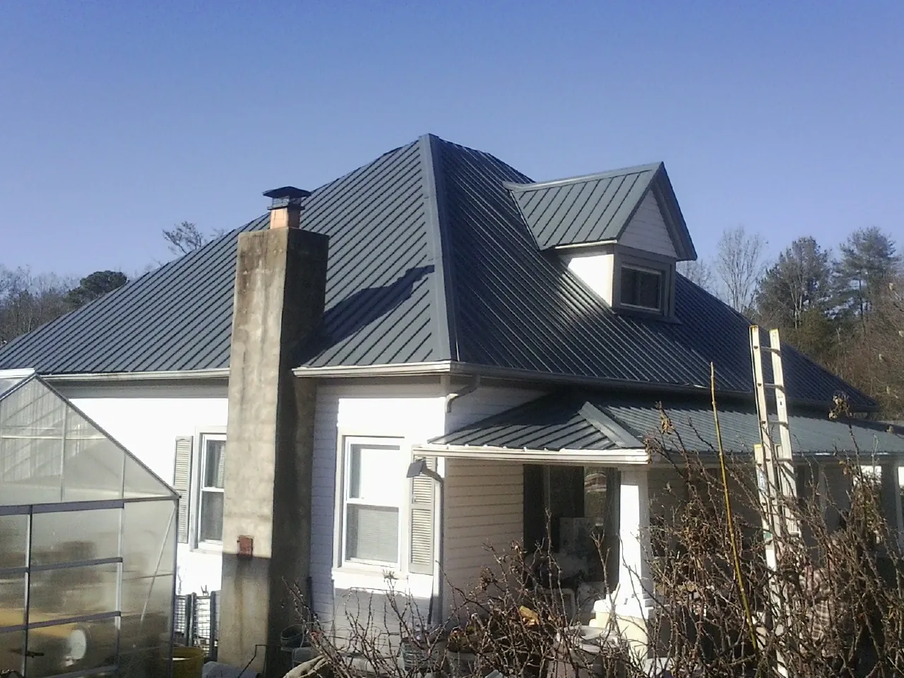 Dark blue standing seam metal roof on a white farmhouse with dormer — Slate & Tile Roof Repair by Roofing Brothers in Cheney