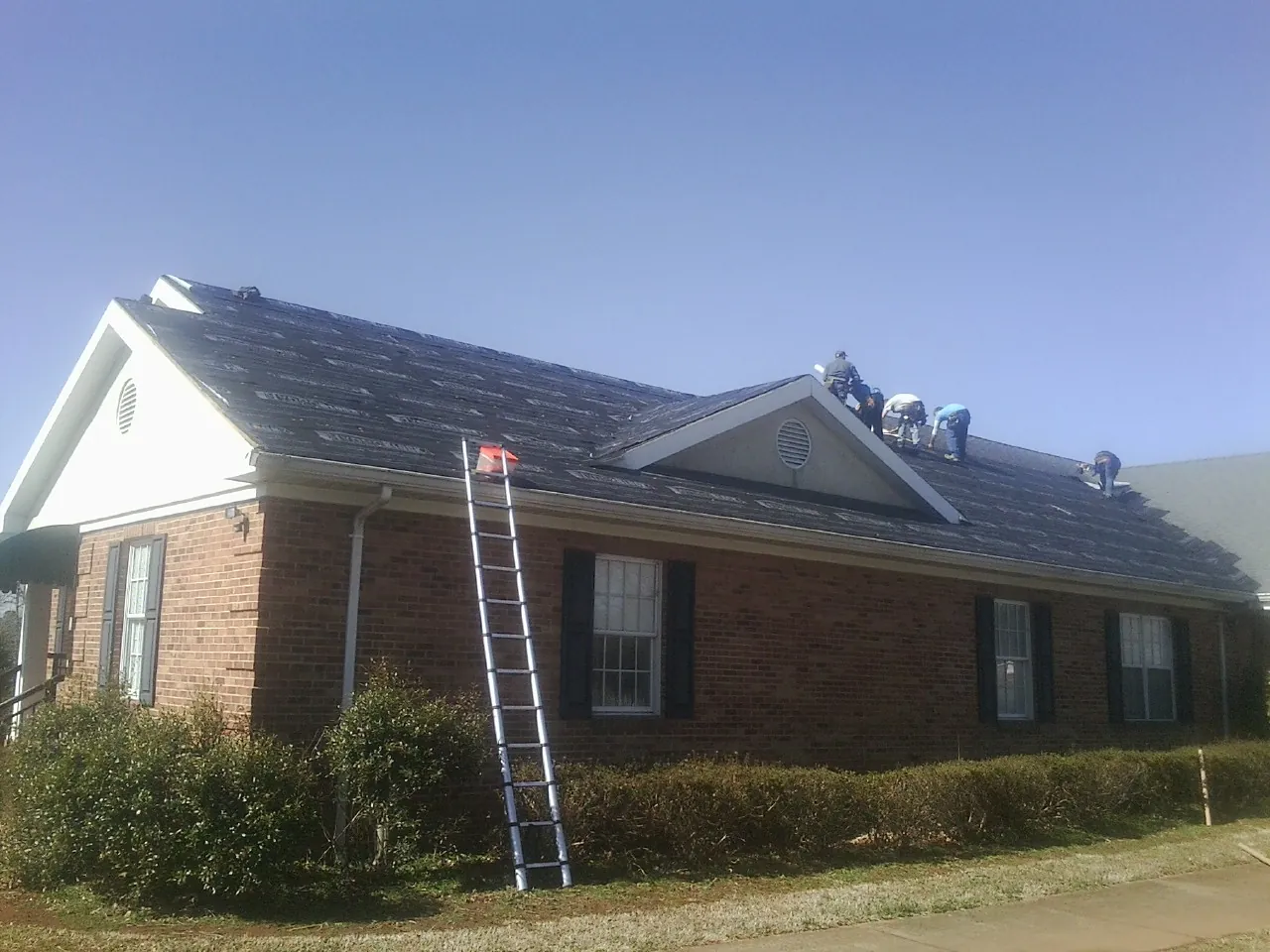 Crew tearing shingles off a brick ranch roof with a ladder set — Metal Roof Repair work by our crew in Cheney