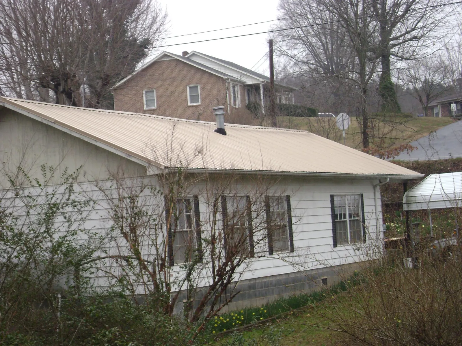 Tan metal roof on a white sided house set into a hillside — Commercial Roofing by Roofing Brothers in Cheney